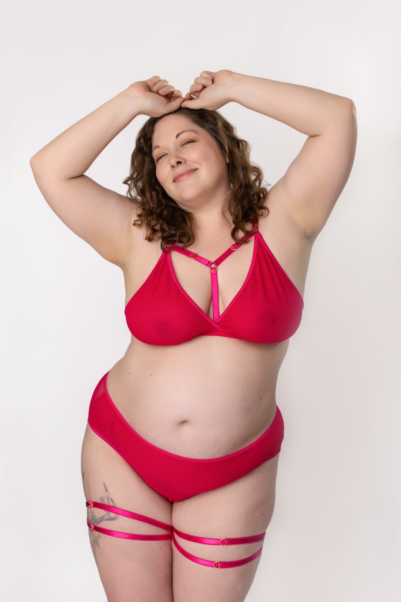 Plus-size woman posing in hot pink lingerie set with arms above her head