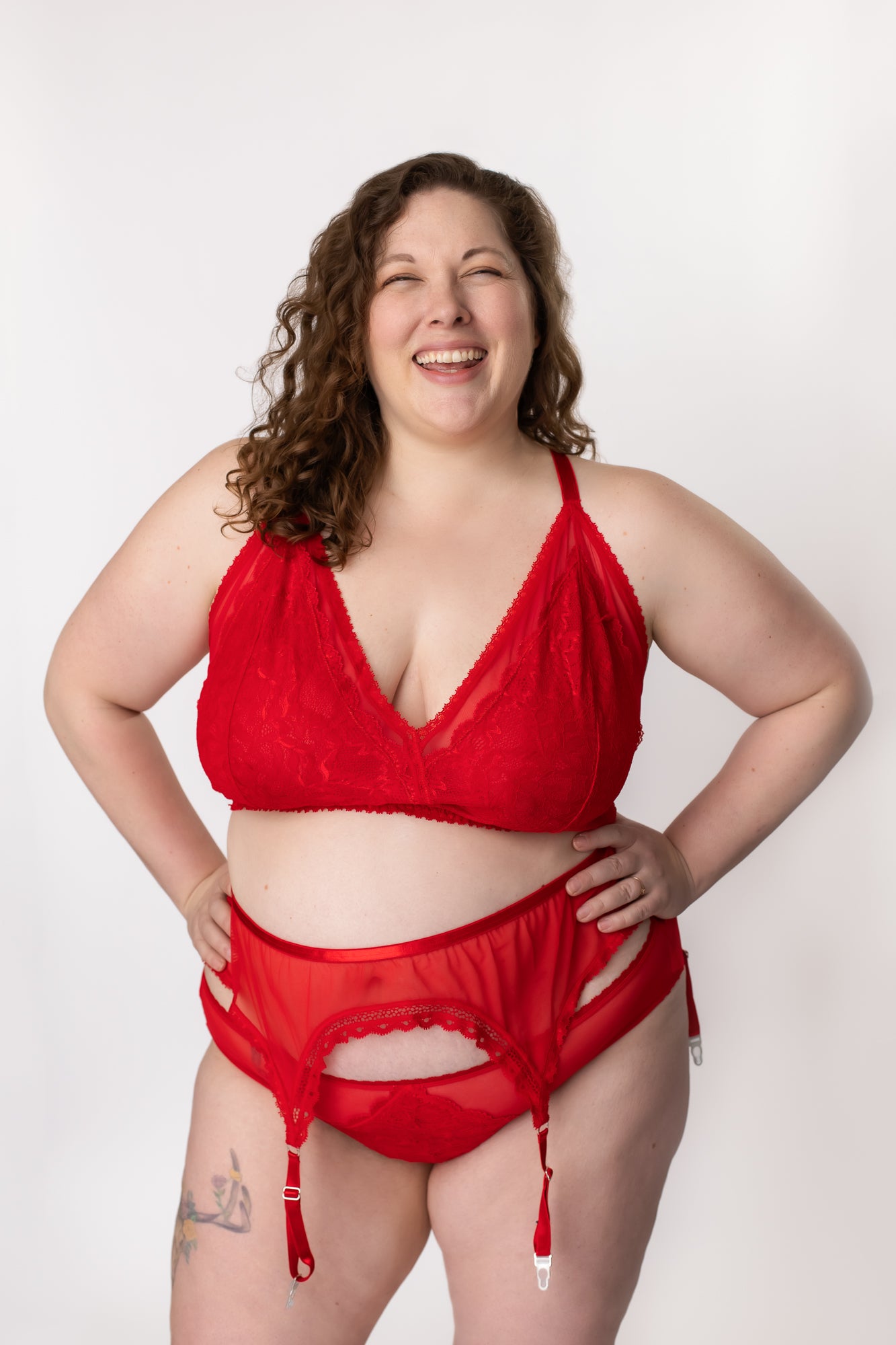 Woman laughing while wearing a red lace and mesh bralette and panty with a matching garter belt