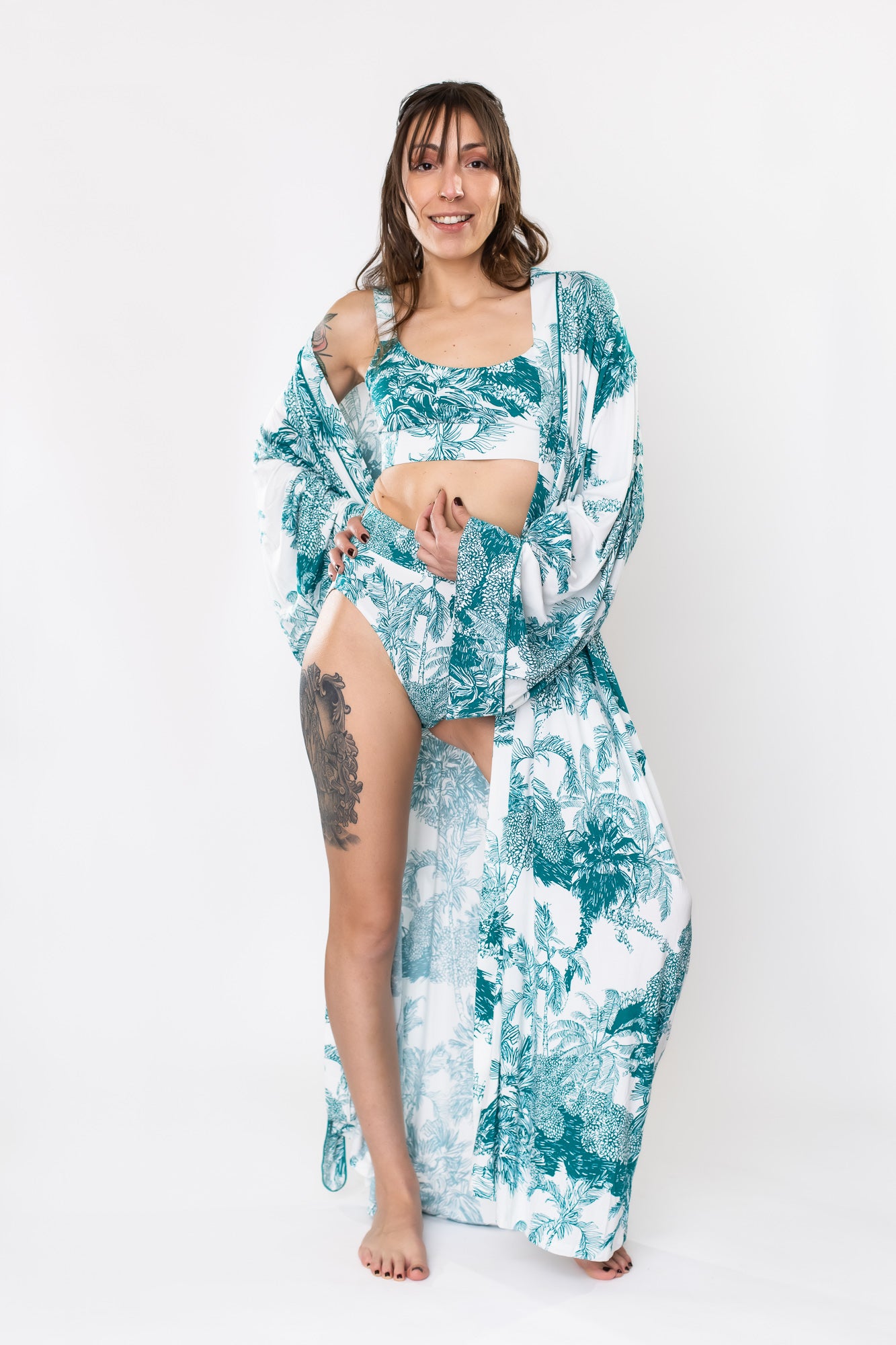 Woman standing in a lounge set with a bamboo bralette, brief, and robe with teal palm leaf pattern