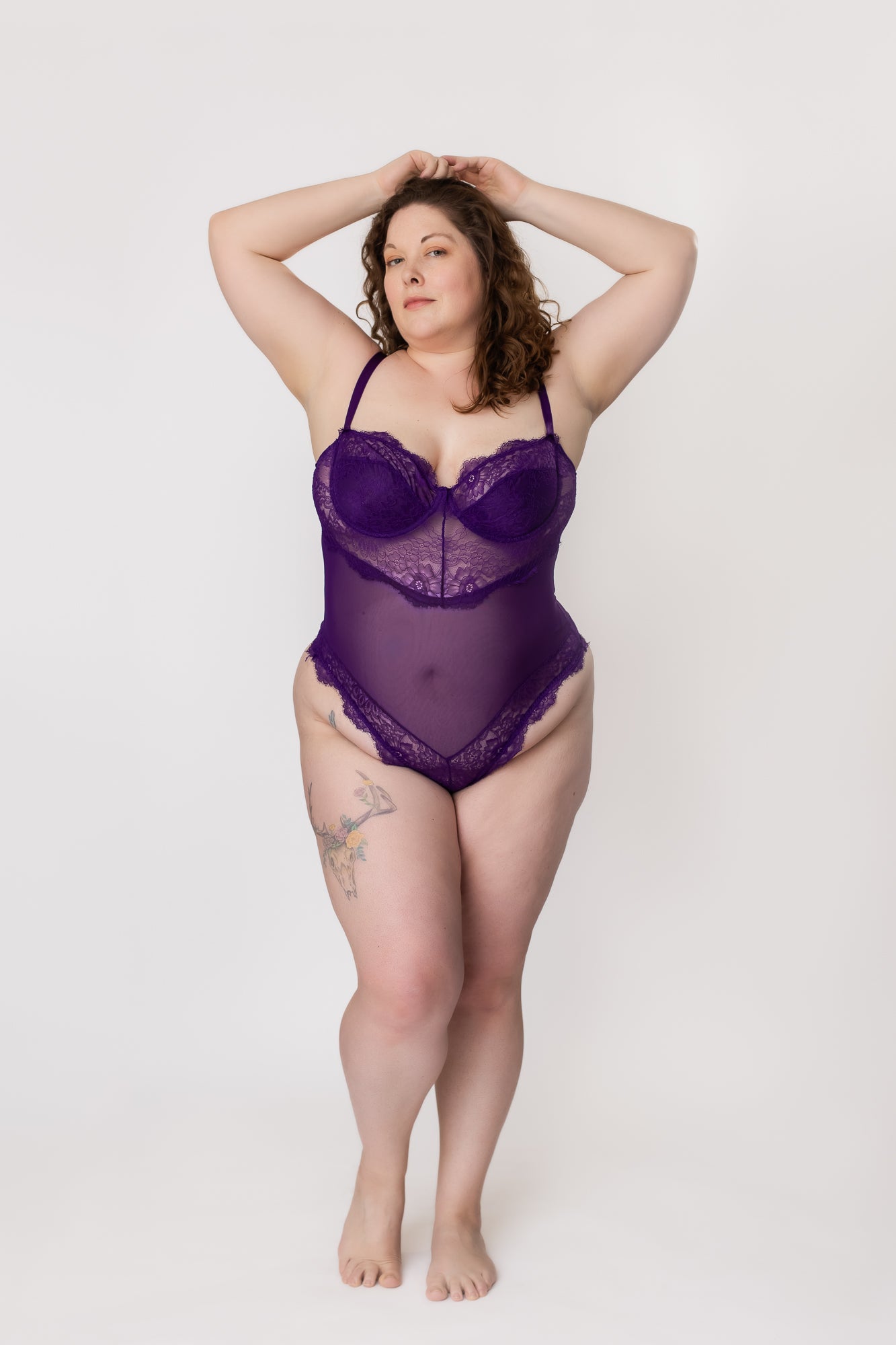 Plus-size woman standing in a purple lace and mesh bodysuit