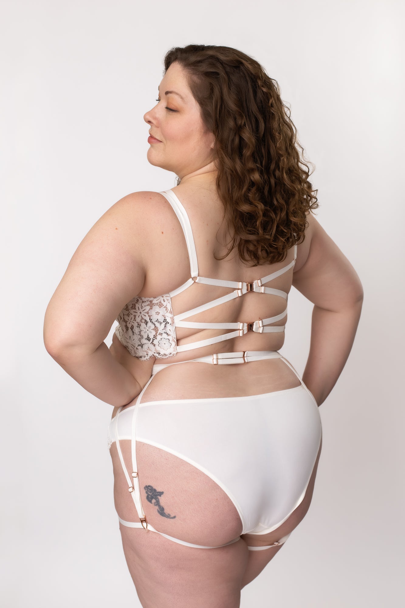 Back view of a woman wearing a plus-size white lace lingerie set with a bustier, panty, and garter belt
